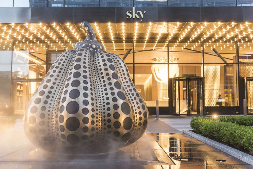 At the forefront of the building, an infinity loop motor court circles an enormous ornamental bronze pumpkin, dotted in black stone––an original work of art by illustrious Japanese artist Yayoi Kusama that was commissioned for Sky